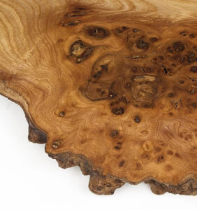 Close-up of an elm burl wood surface, showcasing its rich swirling grain pattern in warm hues. The unique natural design adds elegance and sophistication, making it an ideal choice for fine furniture, decorative accents, and luxury car interiors.
